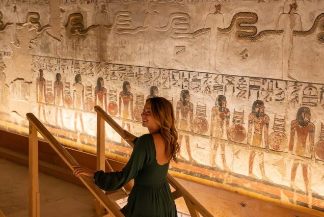 The interior corridor of the tomb of Ramesses IV in the Valley of the Kings, featuring vibrant hieroglyphics on the walls, a wooden visitor walkway, and a magnificent blue astronomical ceiling with golden stars.