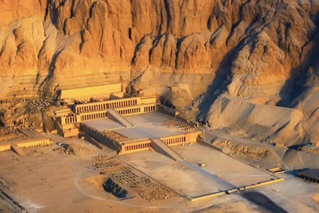 An aerial golden hour view of the Mortuary Temple of Hatshepsut carved into the limestone cliffs of Deir el-Bahari in Luxor.